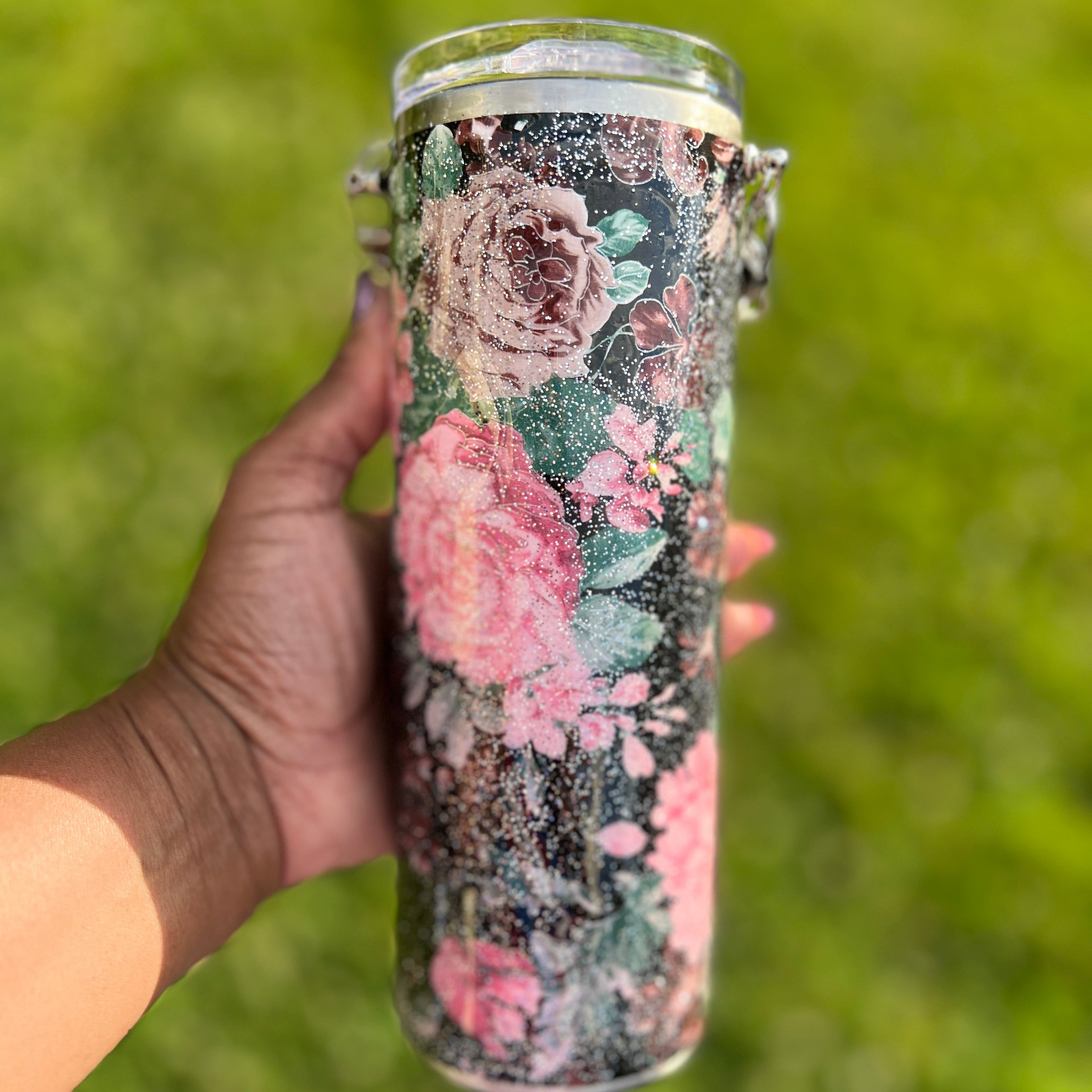 Hand holding a floral-patterned tumbler against a grassy background