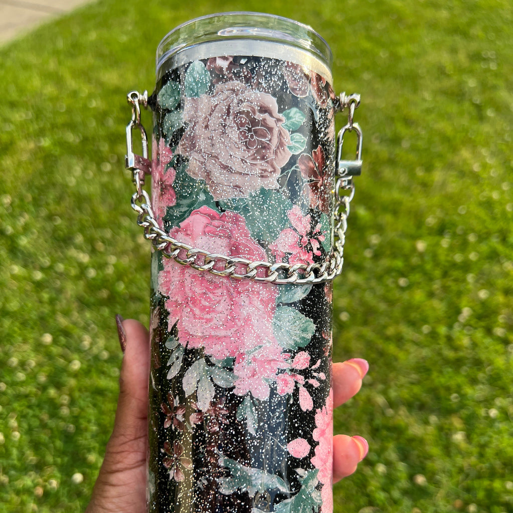 Decorative water bottle with floral design held by a hand against a grassy background